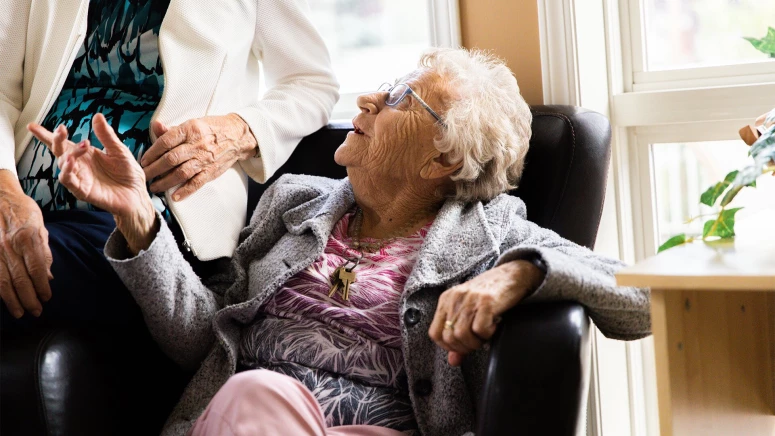 Two senior women sitting on a chair and talking